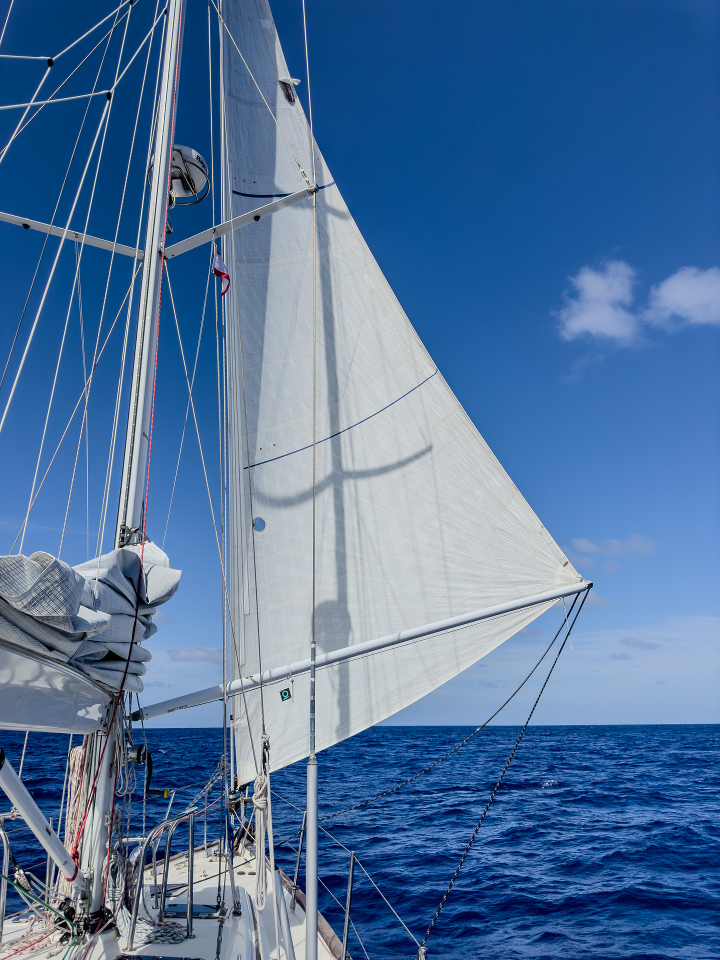 Sailboat with white sails gliding on a deep blue ocean under a clear sky, with rigging and mast visible.