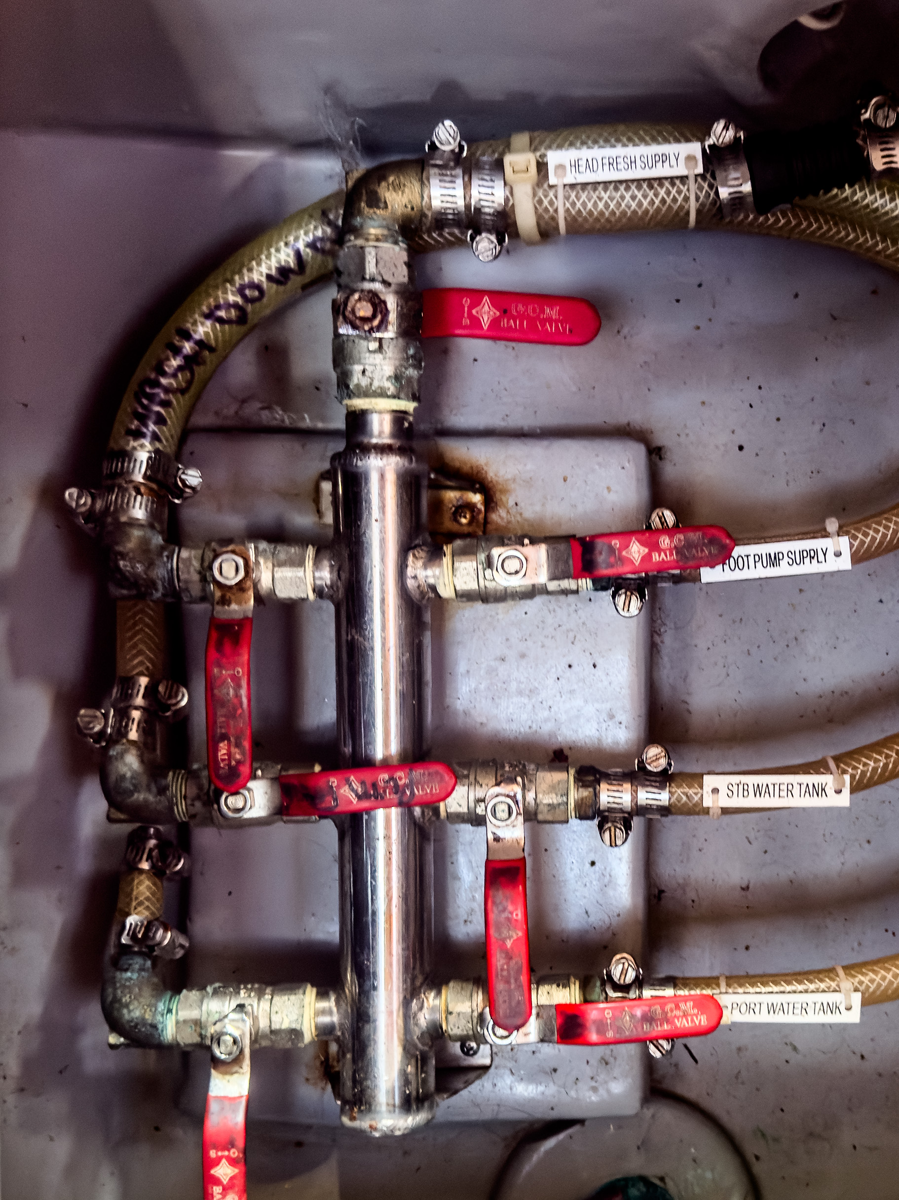 A complex network of metal pipes and red-handled valves, labeled for various water supplies, connected with flexible hoses.