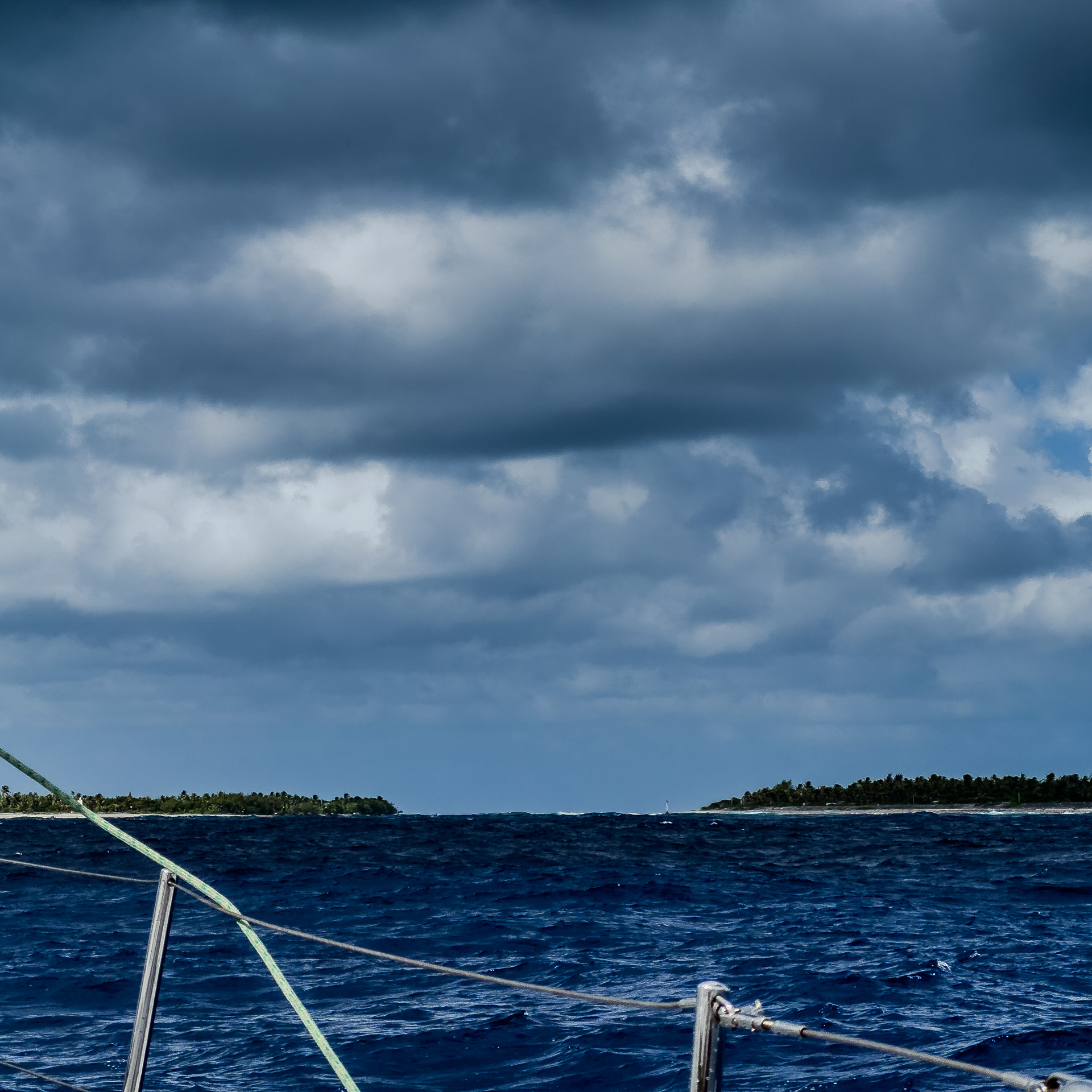 View from a boat showing a deep blue ocean under a cloudy sky, with distant land visible on the horizon.