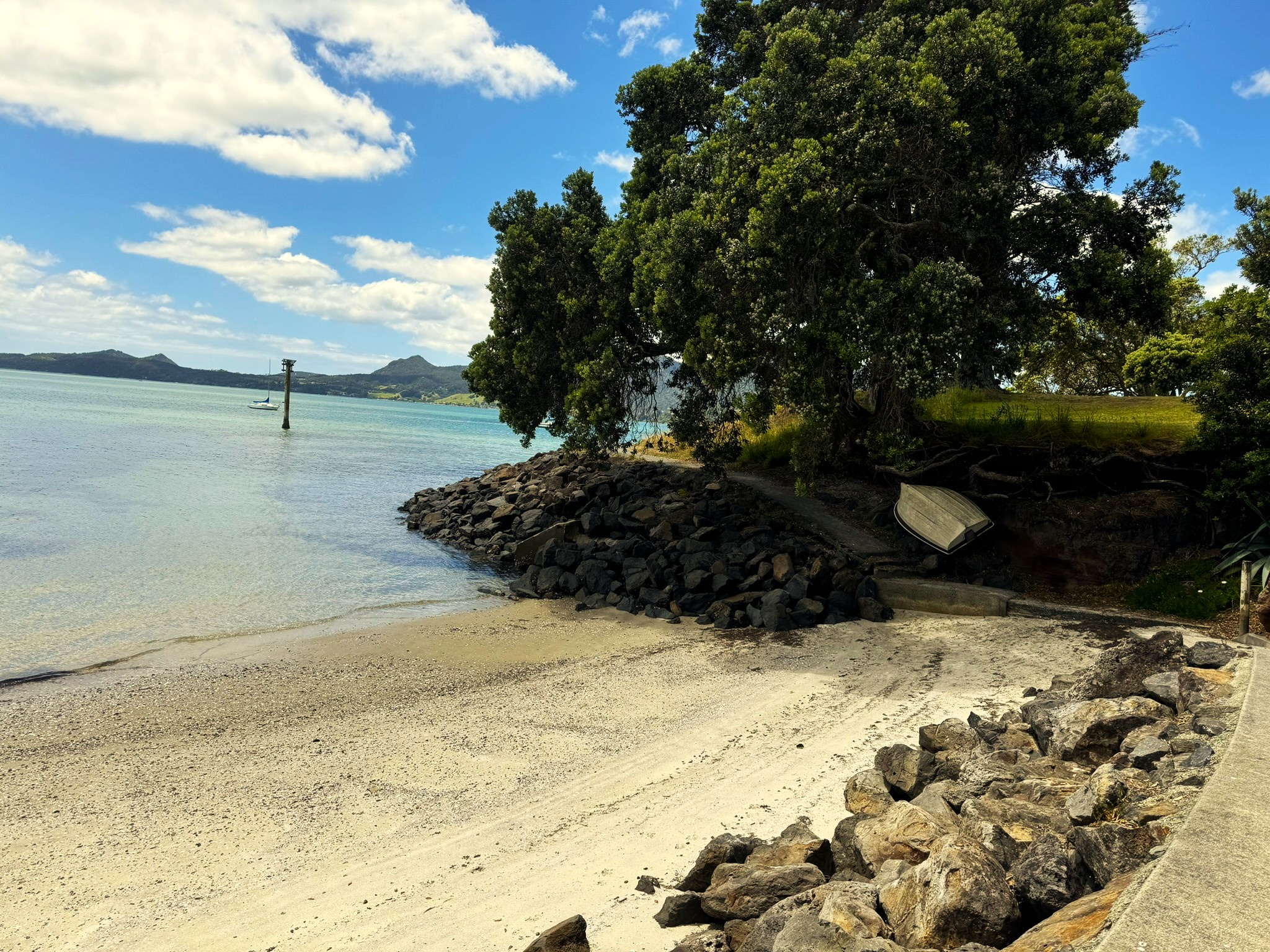 A serene beach in Marsden Cove with calm waters, rocky shoreline, and lush trees under a partly cloudy blue sky.