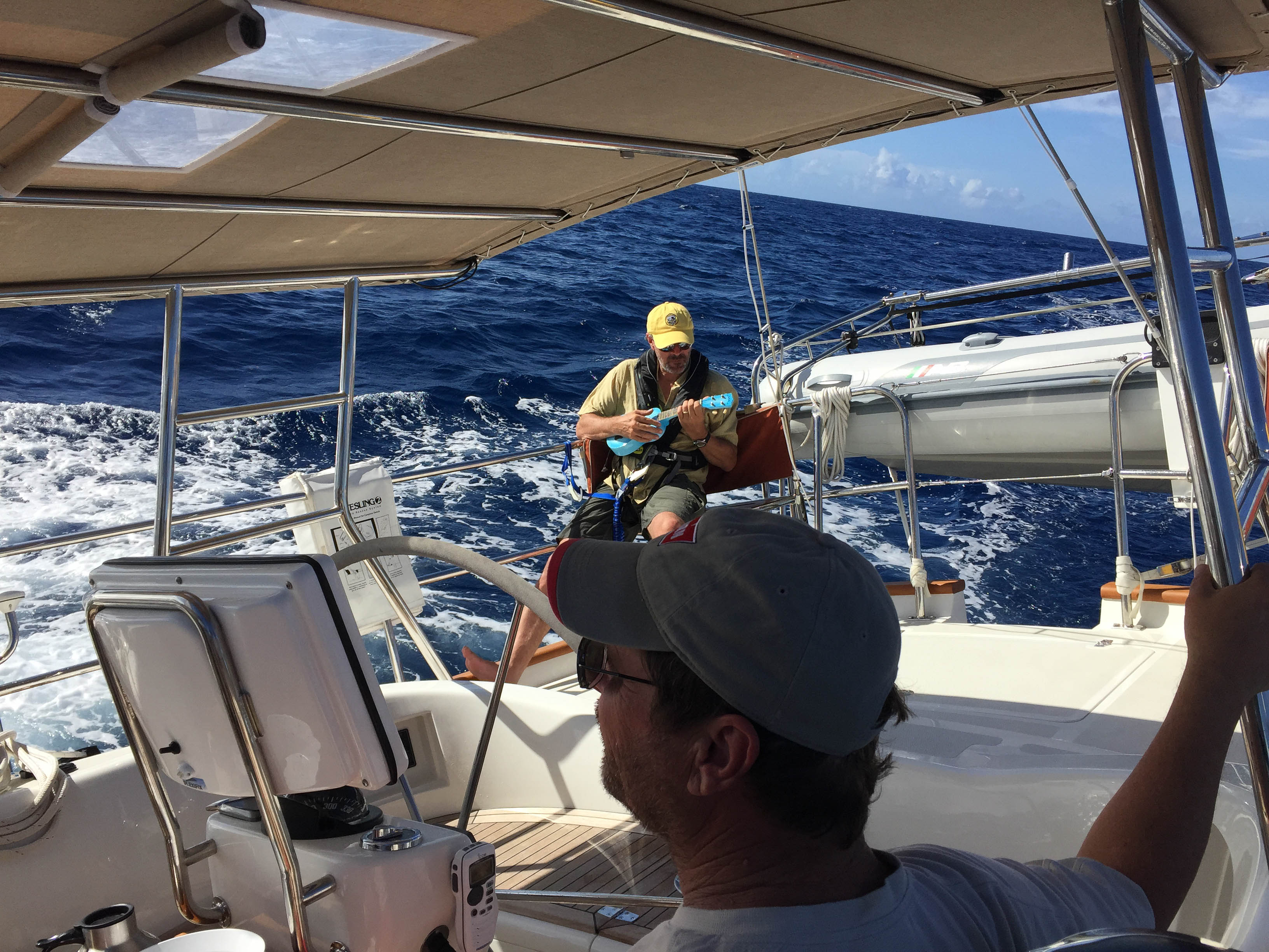 People sailing on a boat in the ocean, one wearing a yellow hat and playing the ukulele, with waves in the background.