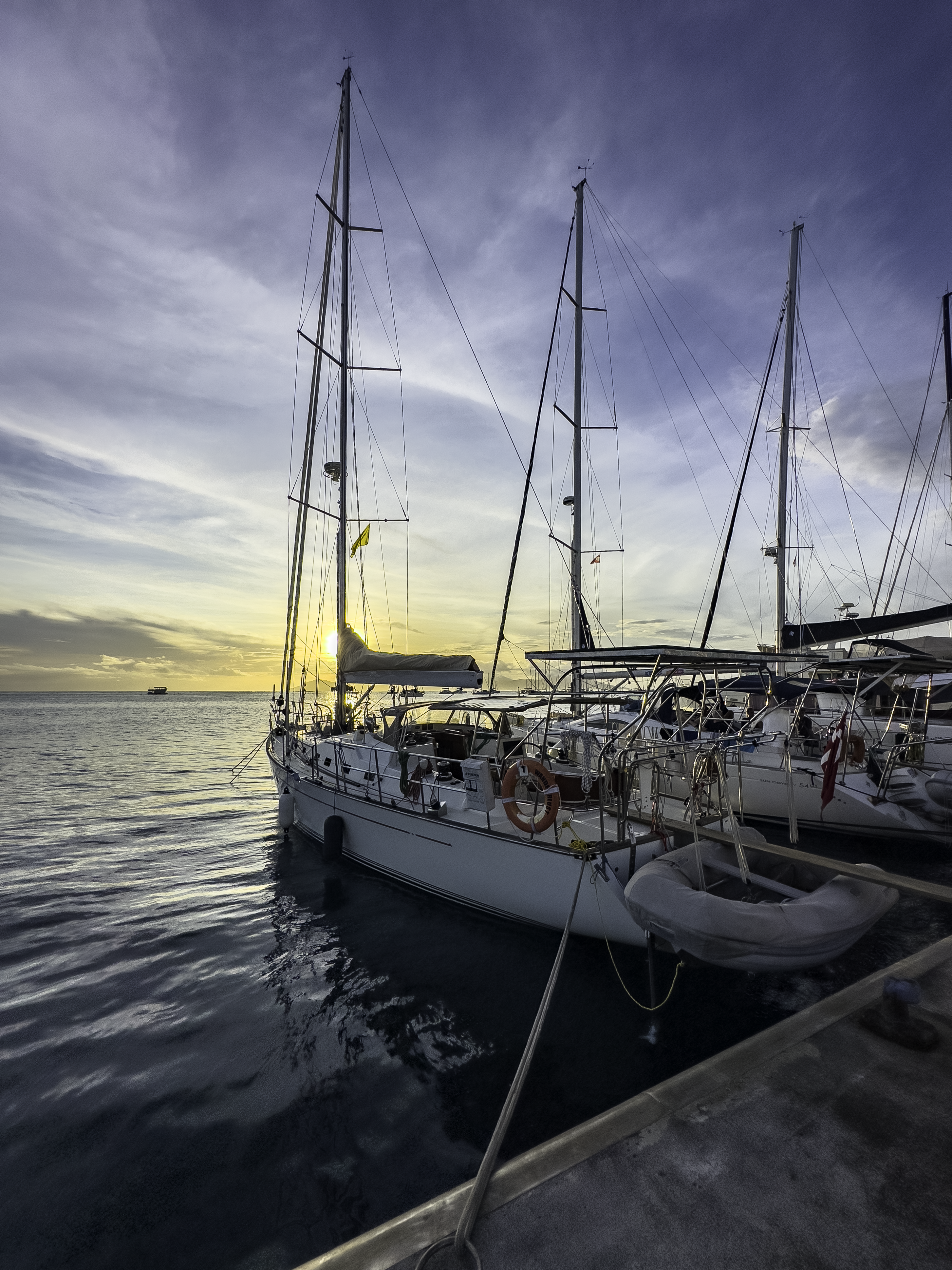 Sailing vessel moored stern to in Marina Taina with the setting sun behind the mast and wispy clouds in the sky