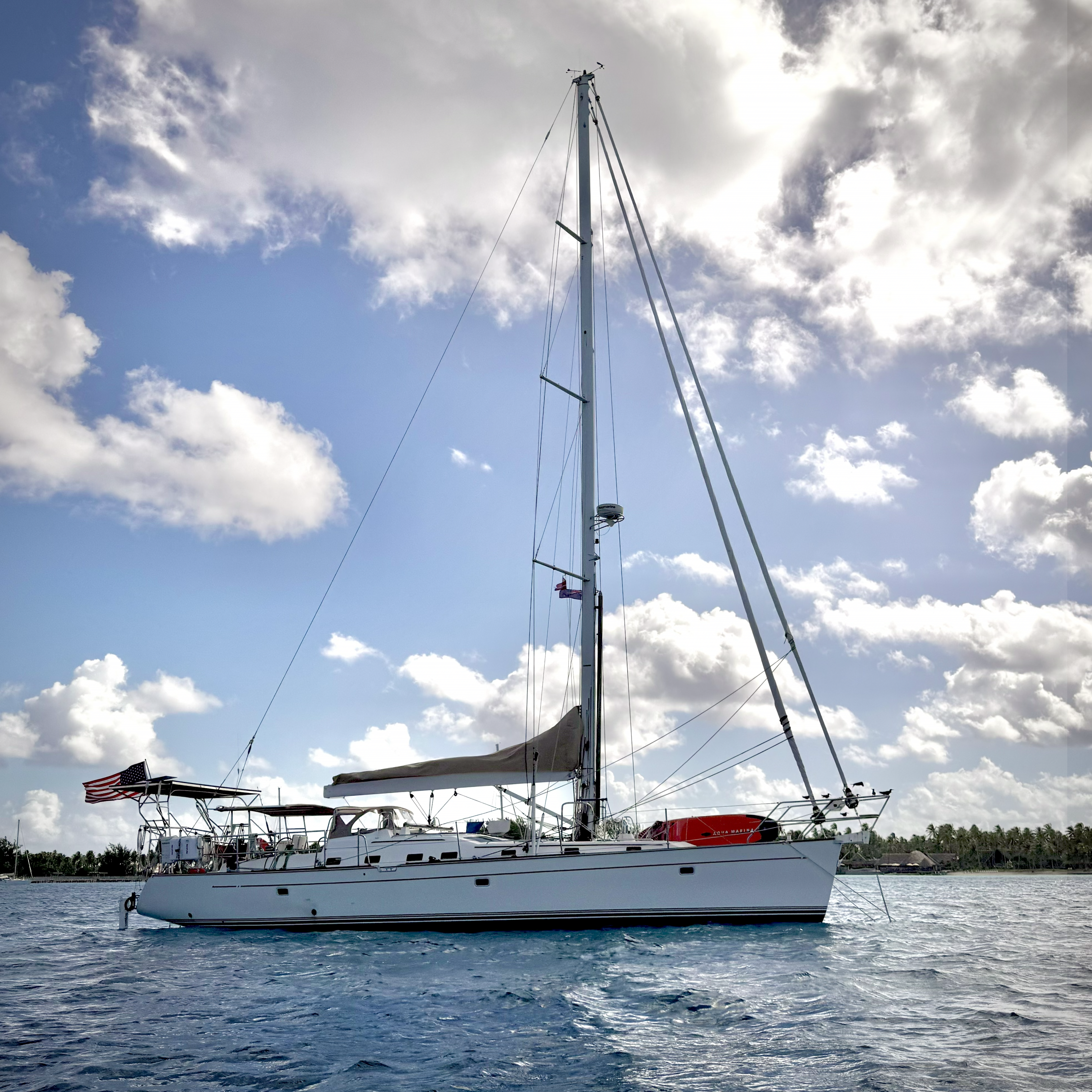 Wanderlust, white sailboat with an American flag laying to an anchor on a calm blue sea under a partly cloudy sky.