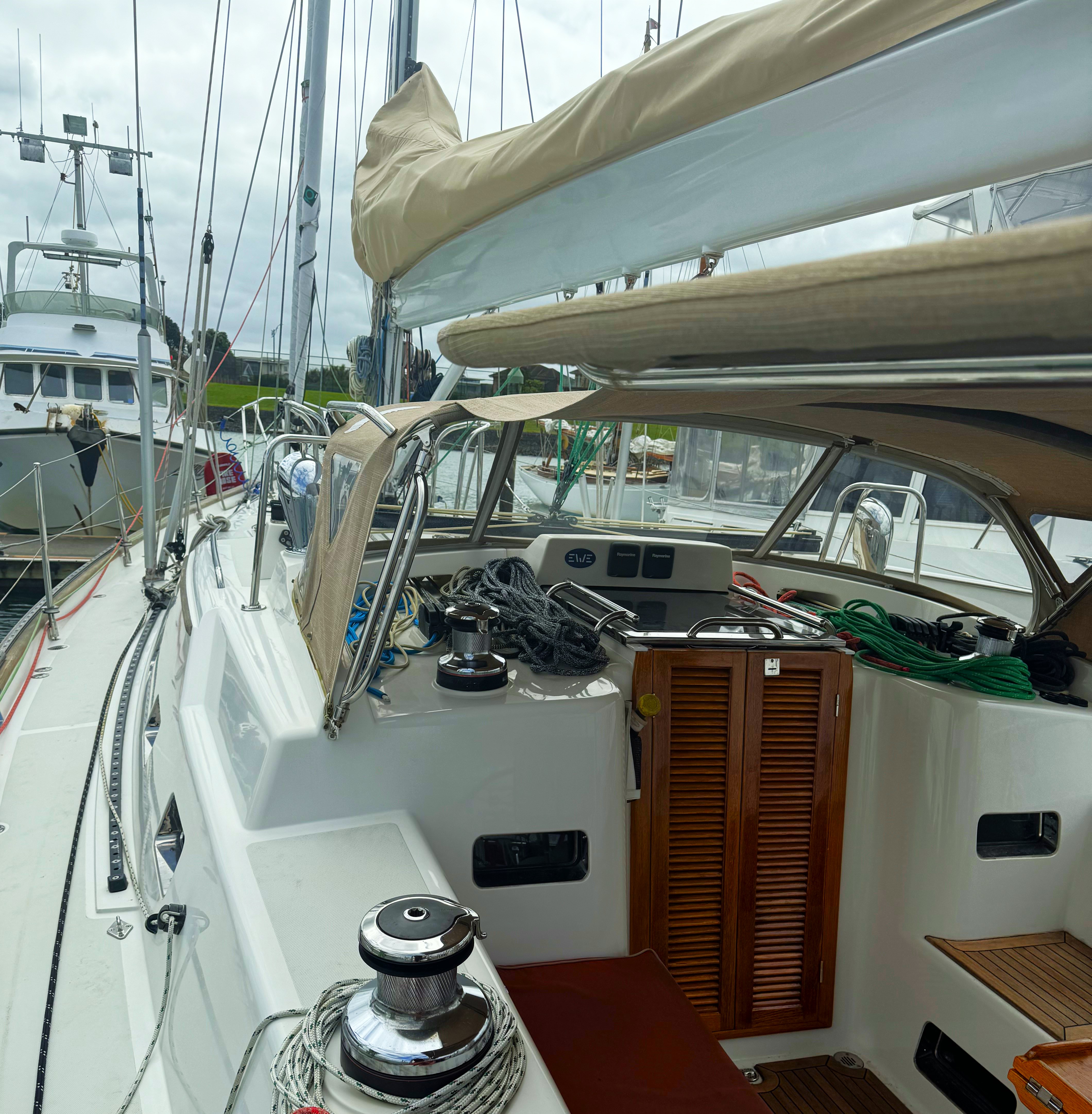 Cockpit of sailboat Wanderlust with wooden doors, winches, and ropes. The deck is equipped with a beige canopy. Other boats are visible in the background.