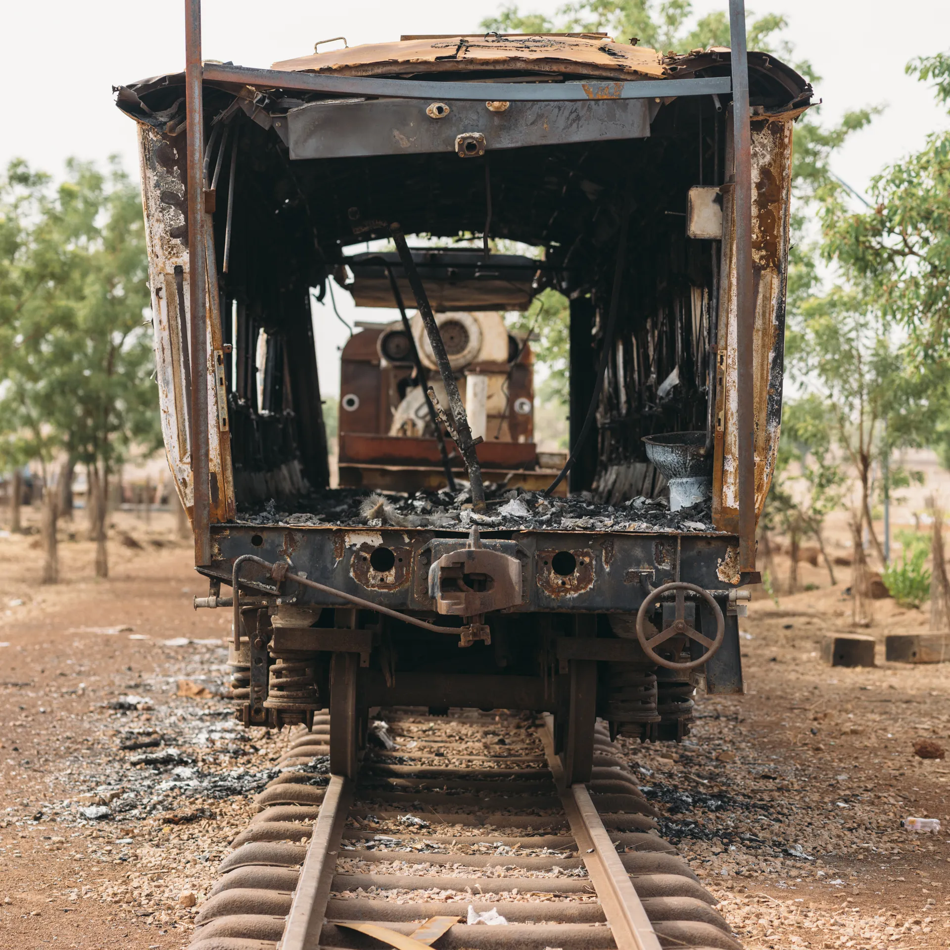 Front view of an abandoned, rusted train carriage on old tracks in a barren landscape with scattered trees in the background.