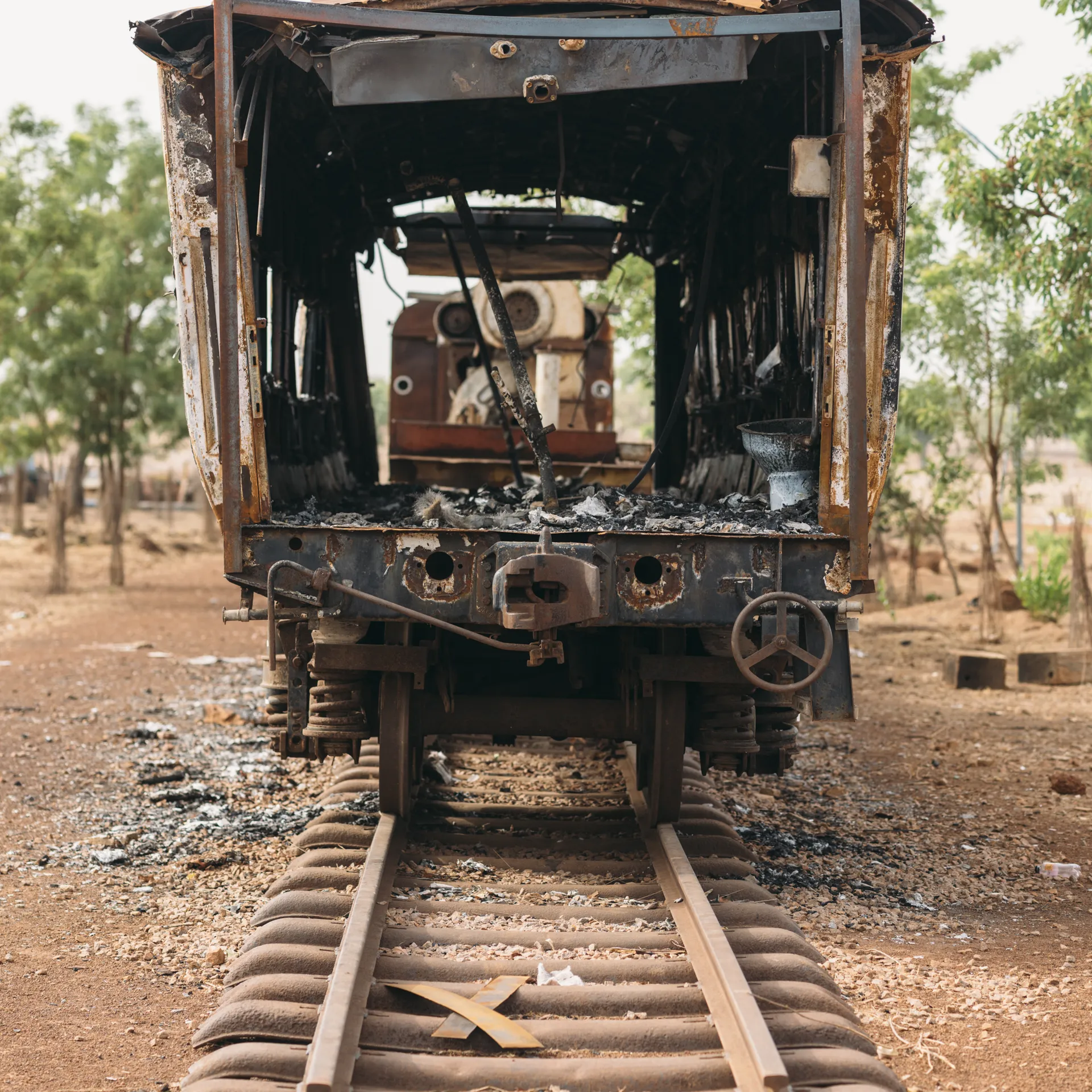 Front view of an abandoned, rusted train carriage on old tracks in a barren landscape with scattered trees in the background.