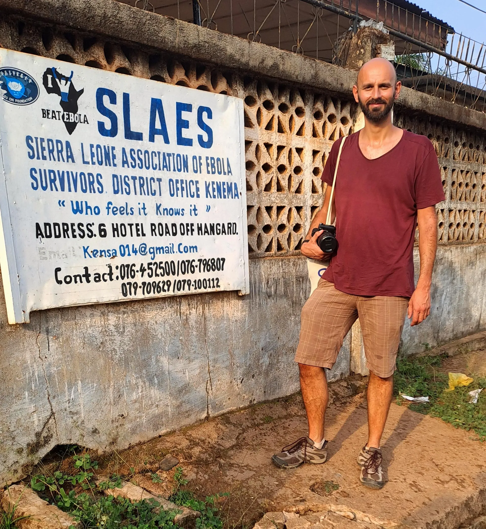 Riccardo standing next to SLAES in Kenema with his camera