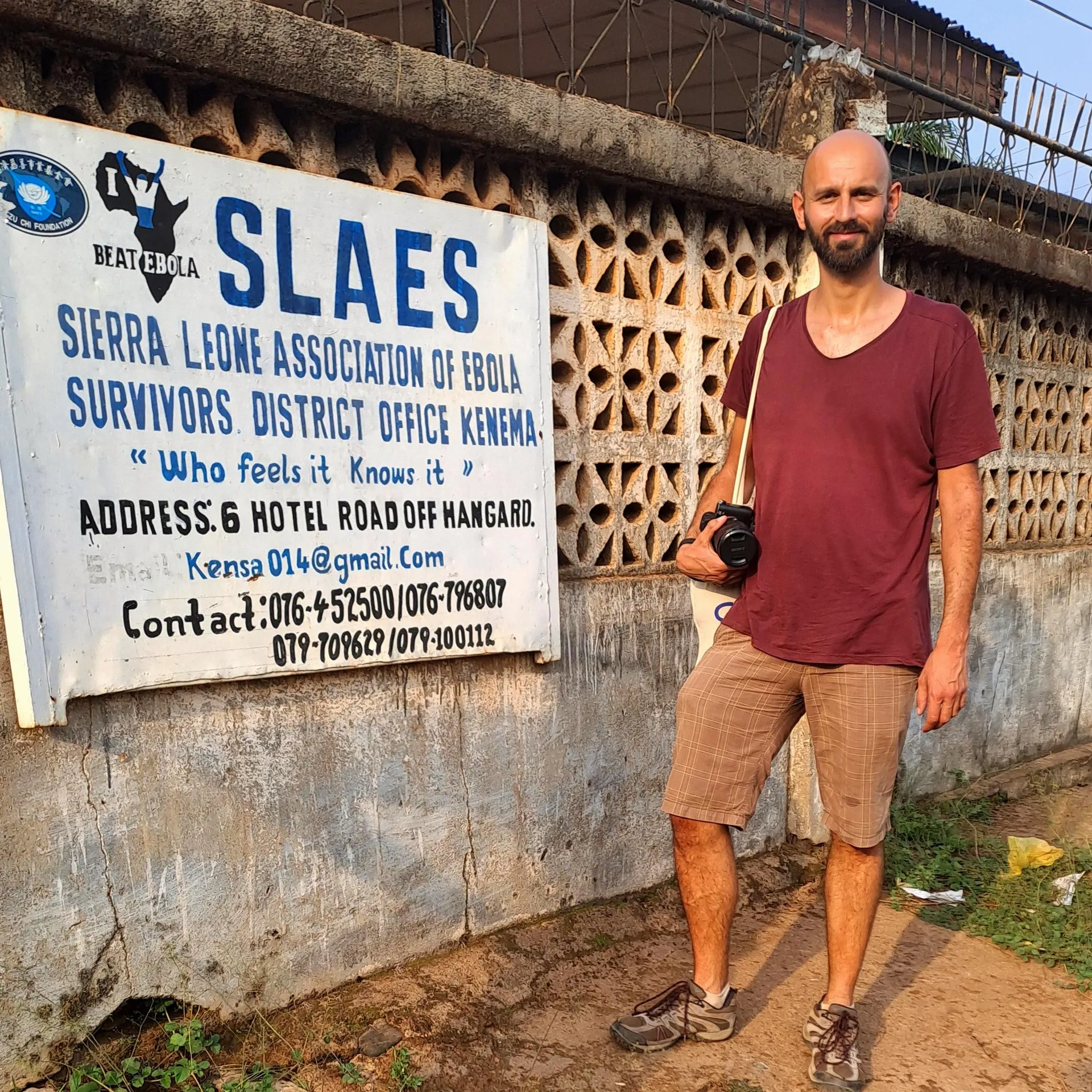 Riccardo standing next to SLAES in Kenema with his camera