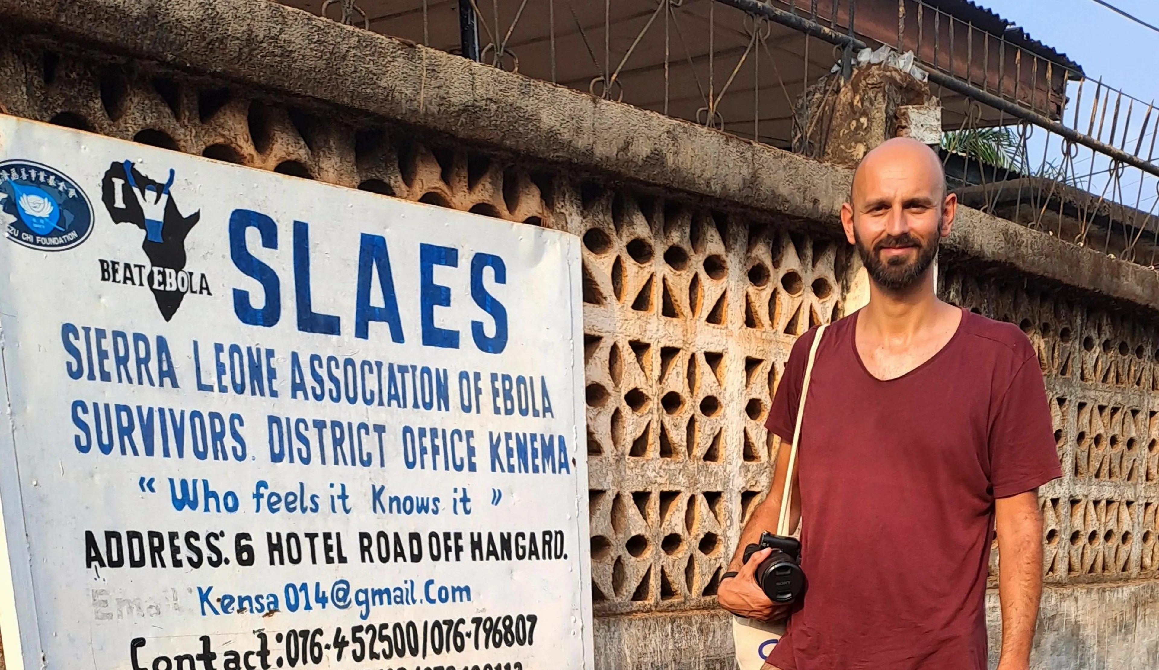 Riccardo standing next to SLAES in Kenema with his camera