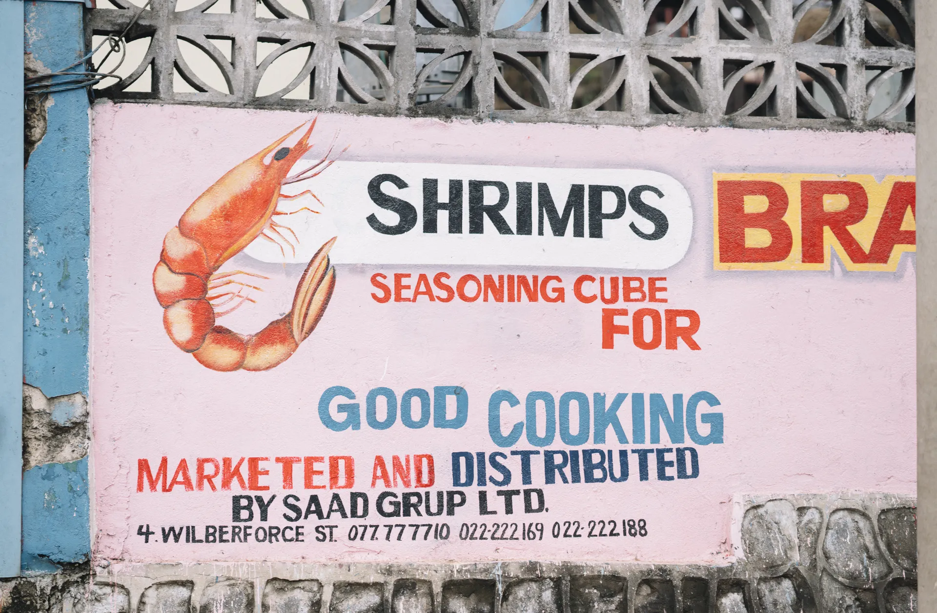 A colorful wall advertisement promoting shrimp seasoning cubes for good cooking, with contact information and decorative shrimp illustration.