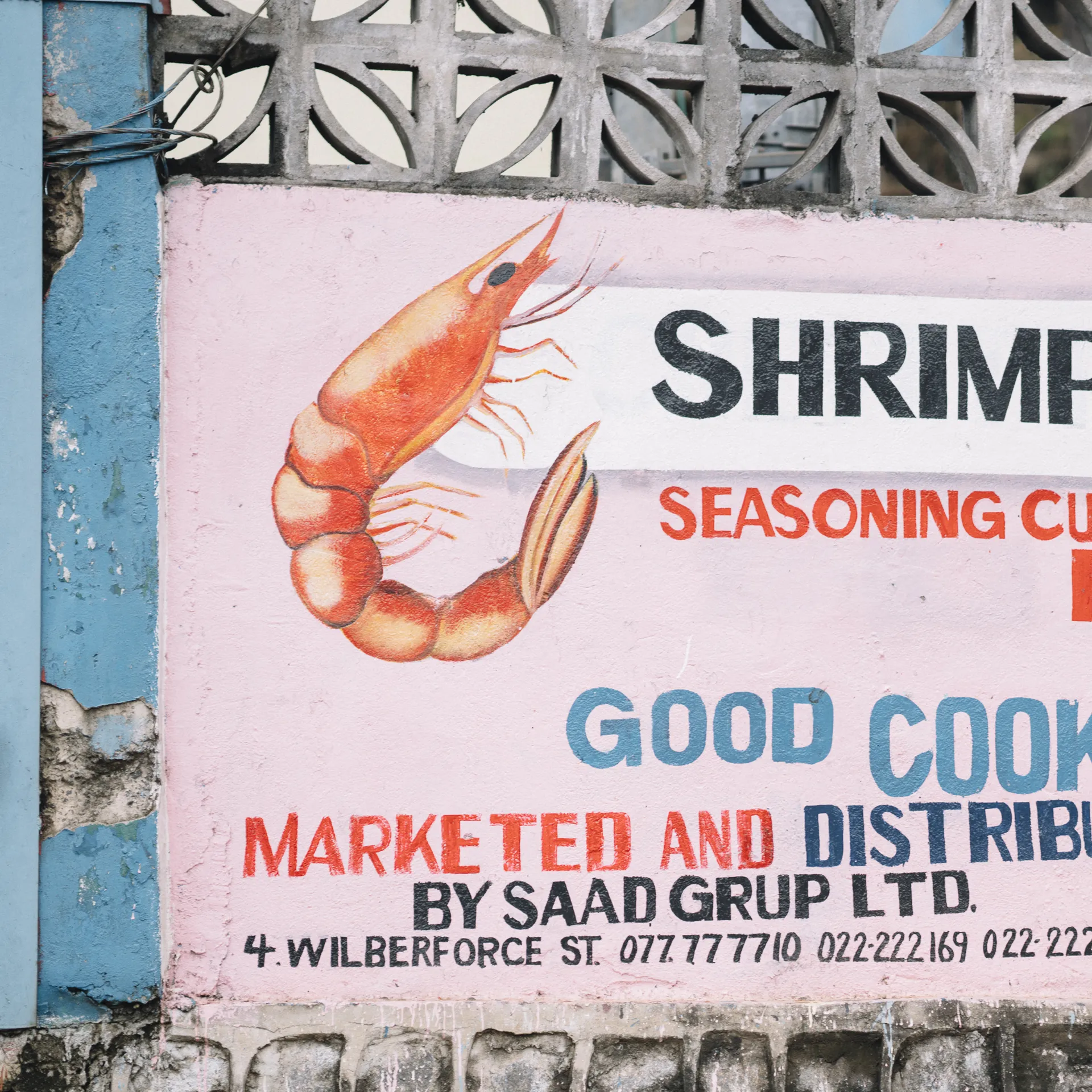 A colorful wall advertisement promoting shrimp seasoning cubes for good cooking, with contact information and decorative shrimp illustration.
