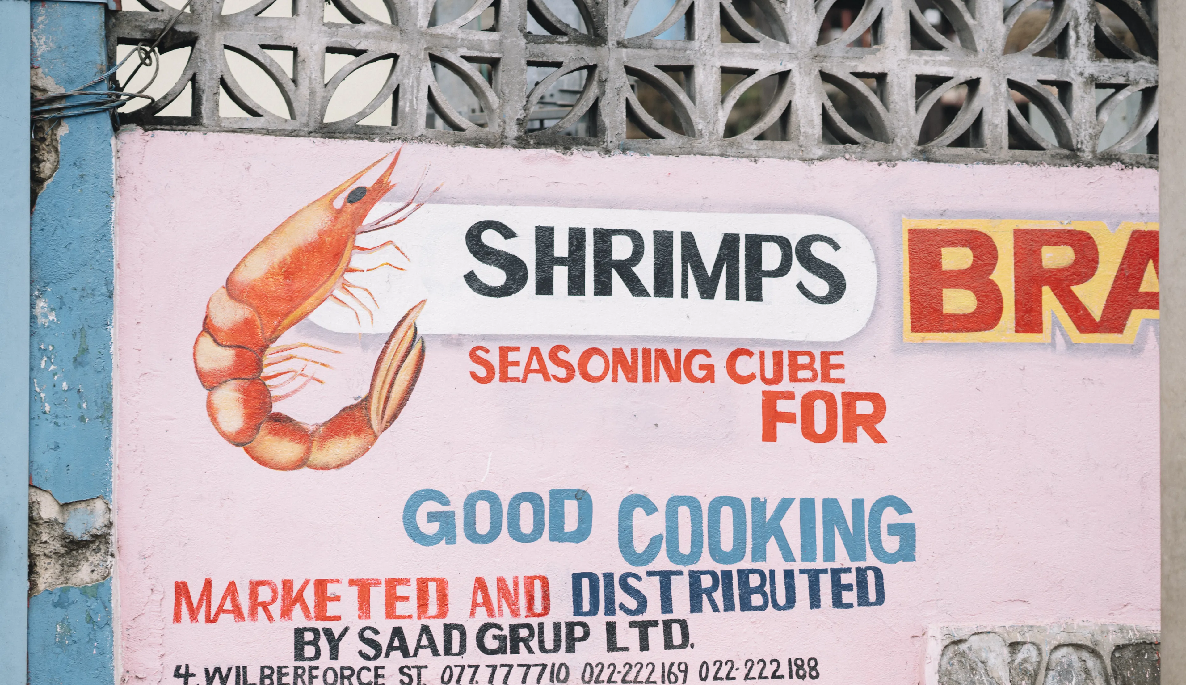A colorful wall advertisement promoting shrimp seasoning cubes for good cooking, with contact information and decorative shrimp illustration.