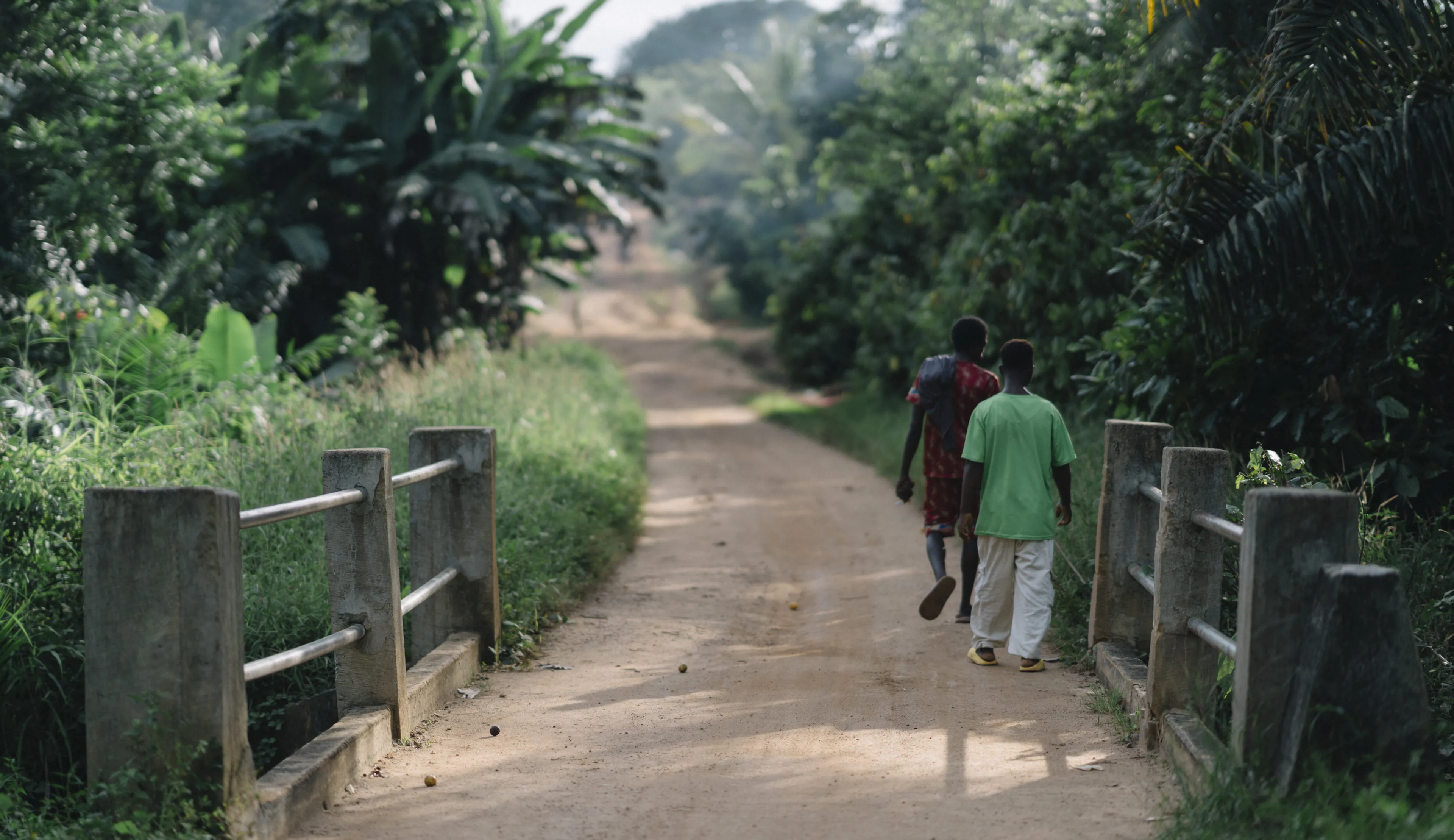 Two people walking down a dirt path surrounded by lush green foliage and concrete fences.