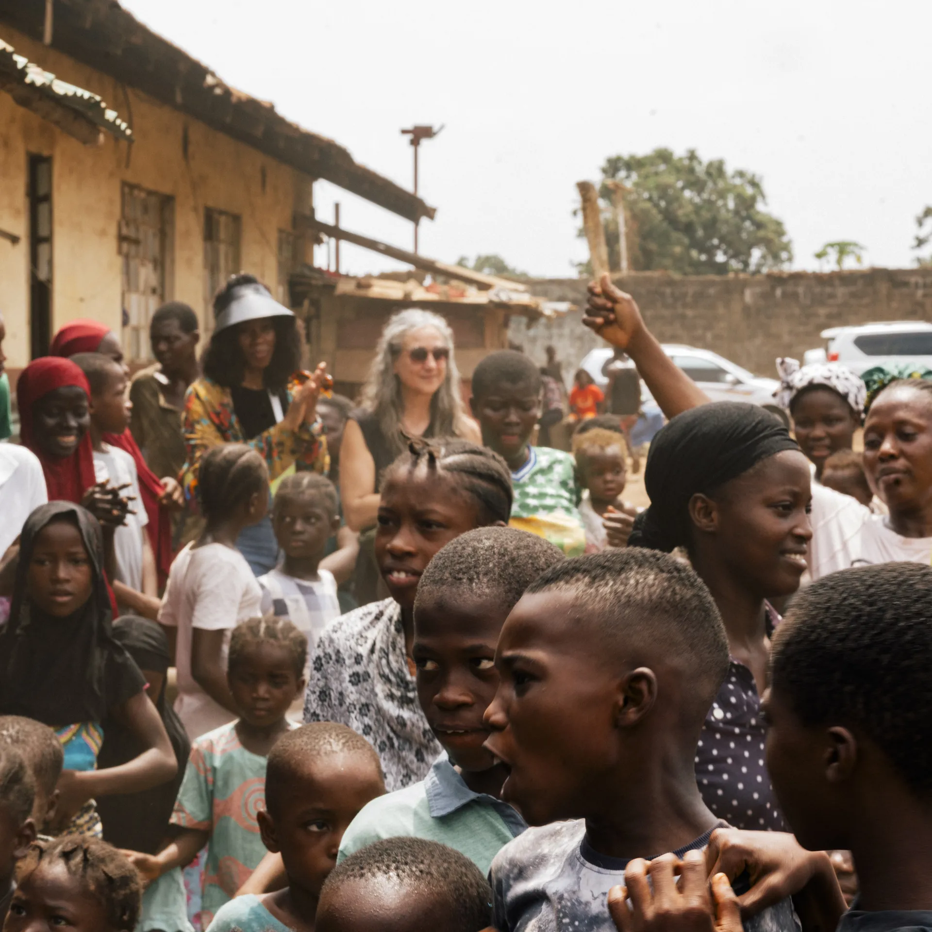 A large group of people, including children and adults, gather outside a building, engaging and interacting with one another.
