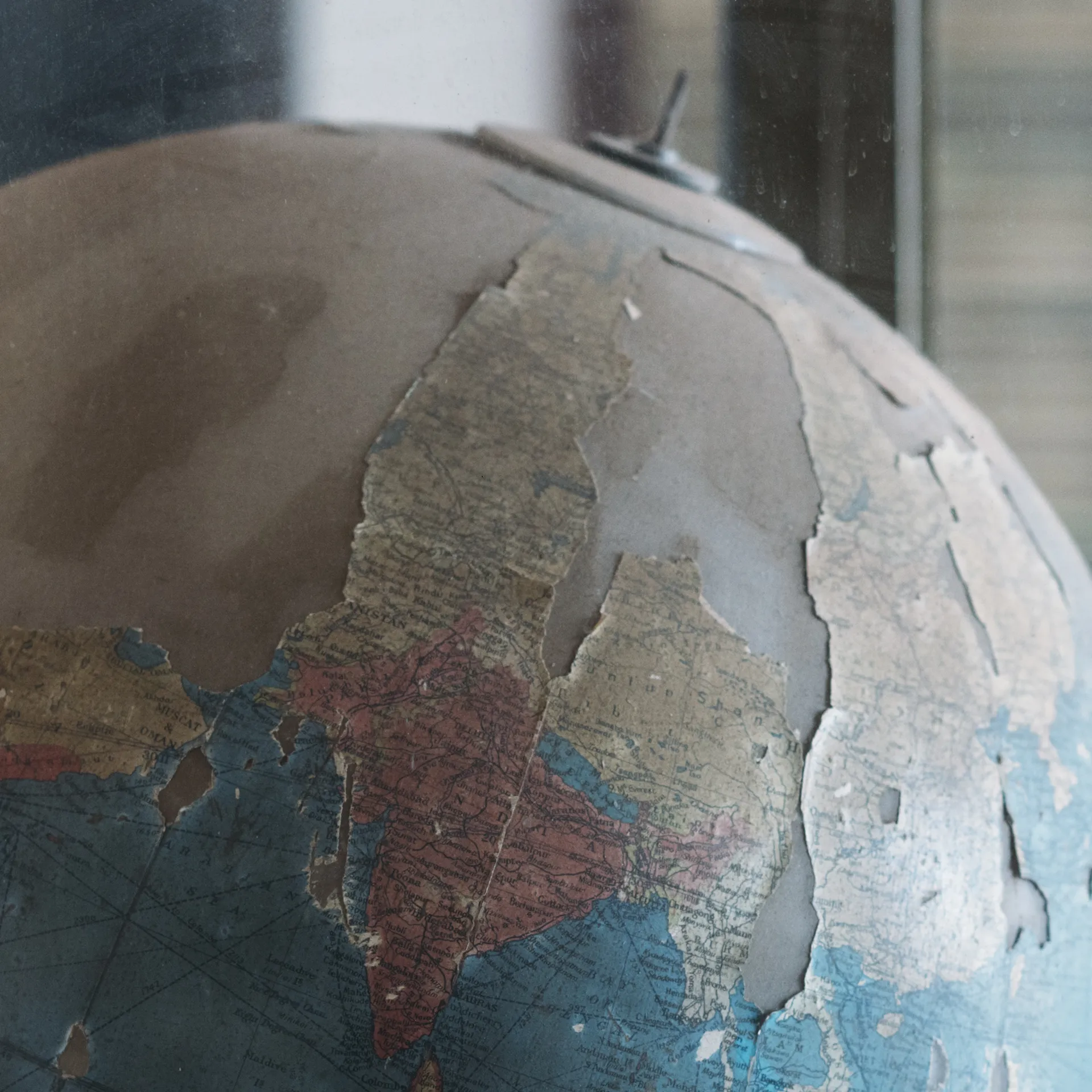 Close-up of a worn,  globe with peeling paper, showing faded blue seas and tan continents, near a blurred background.