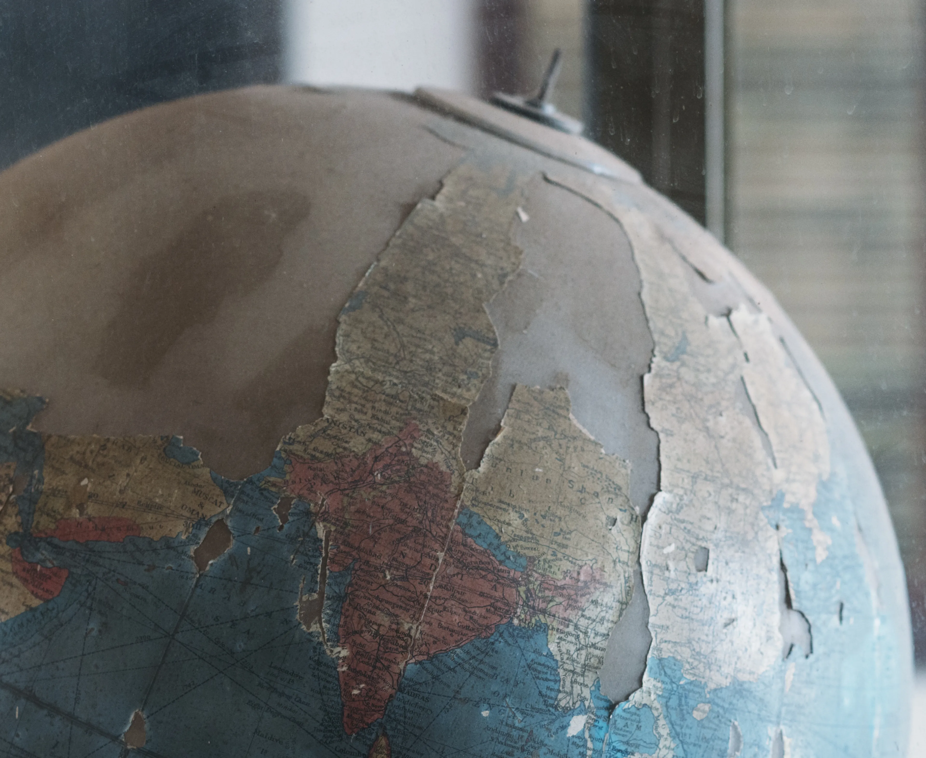 Close-up of a worn,  globe with peeling paper, showing faded blue seas and tan continents, near a blurred background.