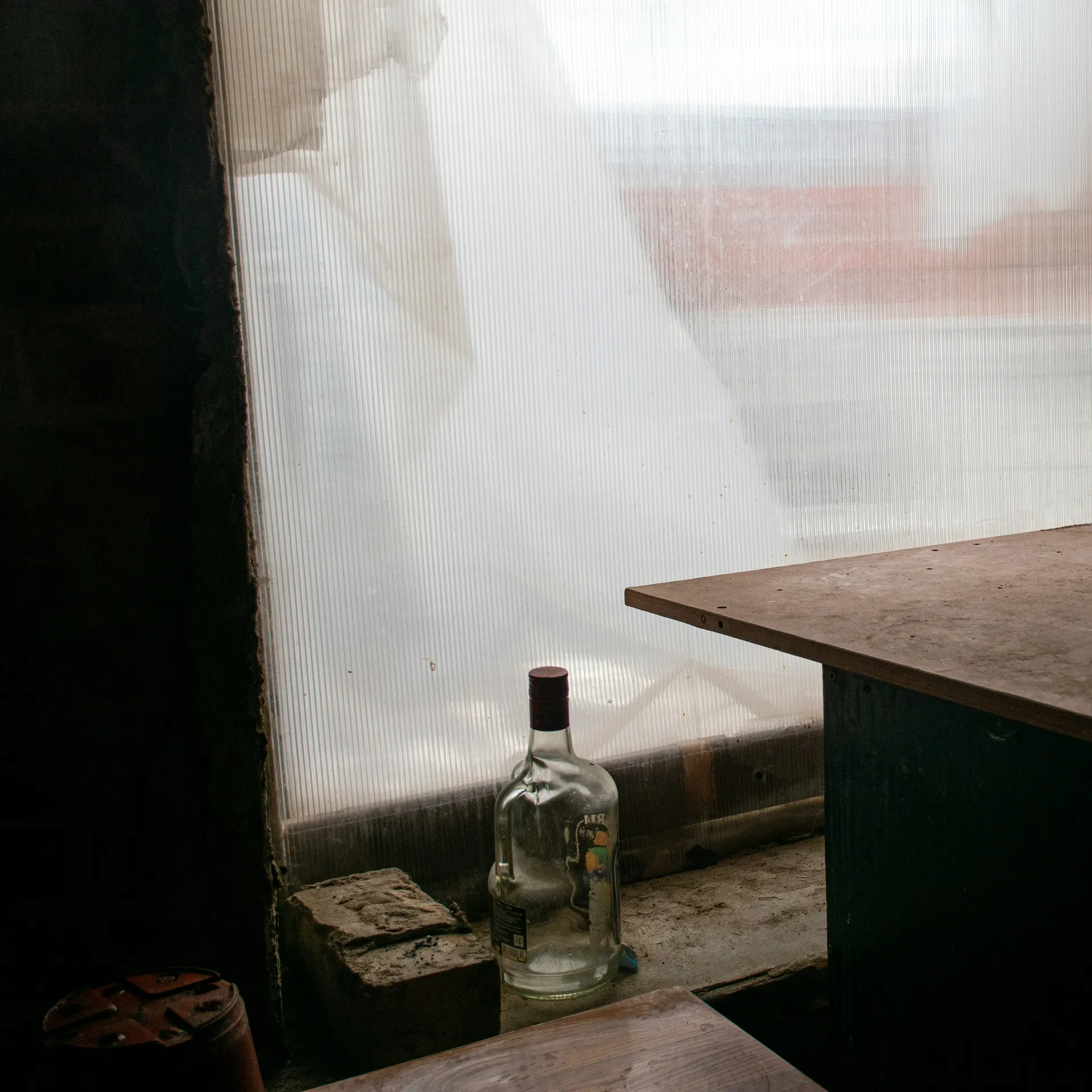 A dimly lit room with a frosted window, a wooden table, and a glass bottle on the ledge, creating a rustic, abandoned atmosphere.