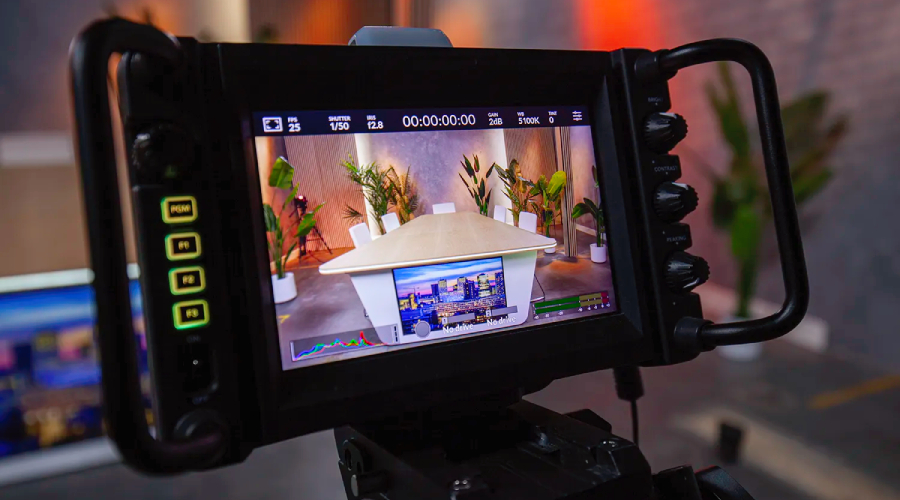 Camera monitor displaying a video of a conference room with a large table, chairs, and potted plants, surrounded by lighting equipment.