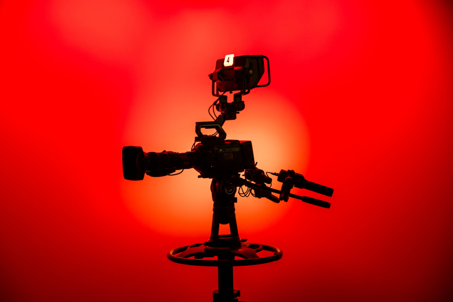 Silhouette of a professional video camera on a tripod against a vibrant red background.