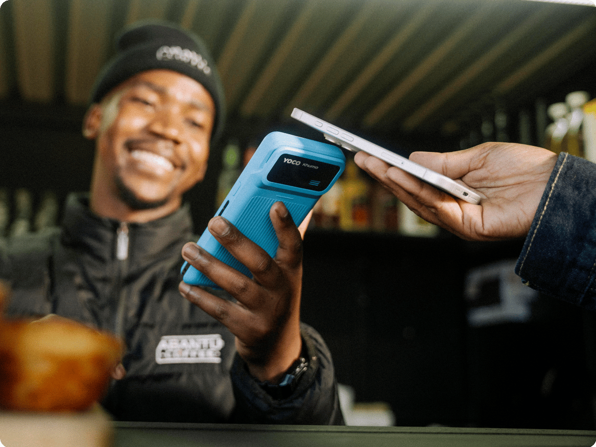 Customer tapping a smartphone on a Yoco card machine to make a contactless payment.