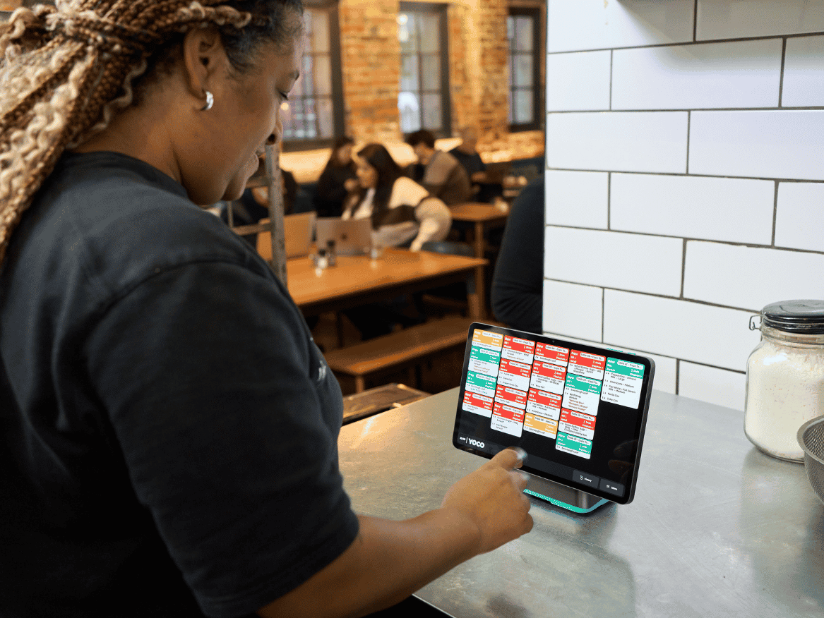 Restaurant employee using a kitchen display showing active customer orders.