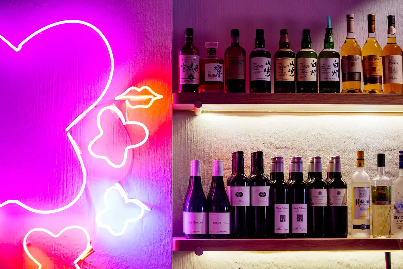 Pink neon artwork beside illuminated shelves of wine and spirits
