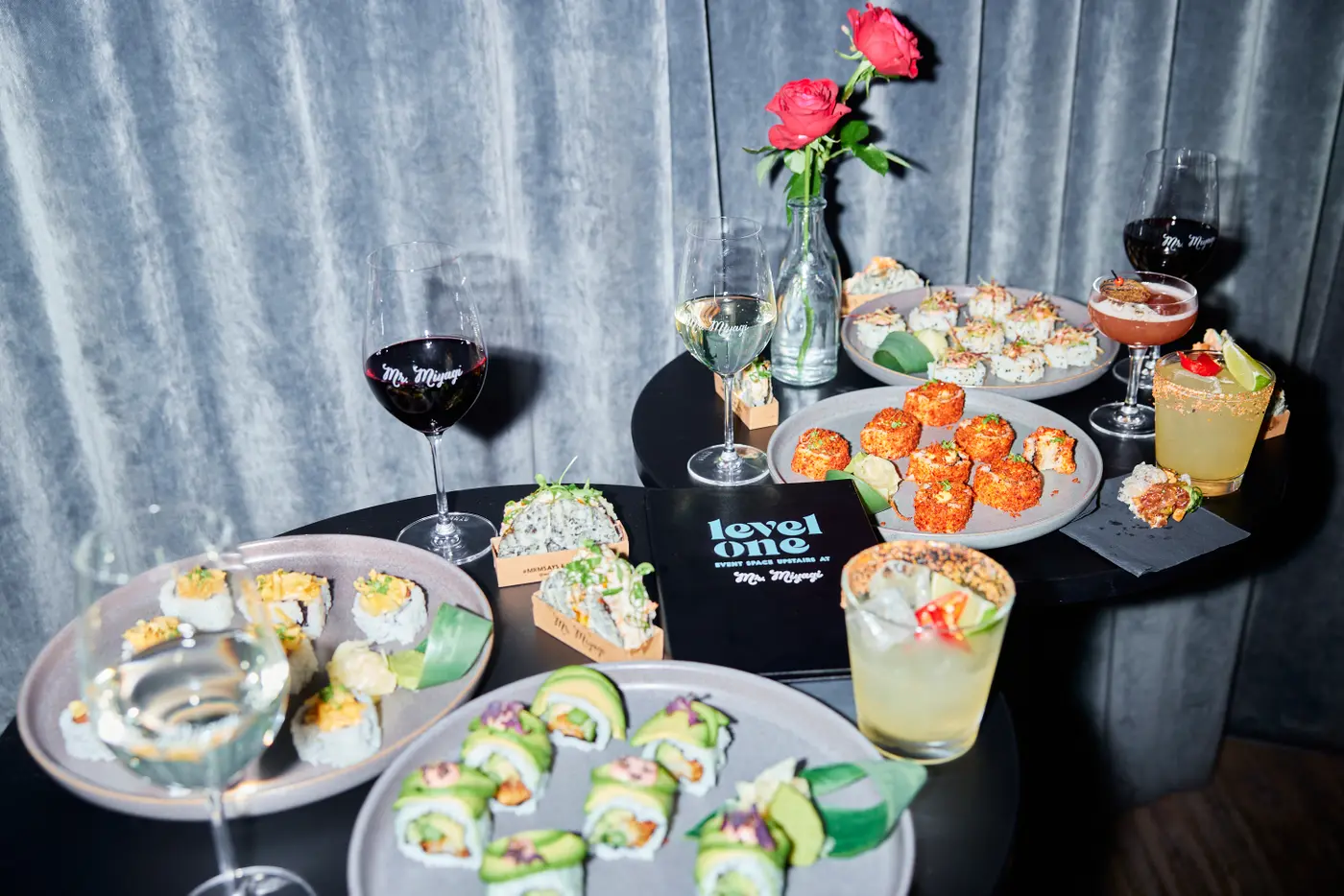 An assortment of sushi, small plates and cocktails on black tables