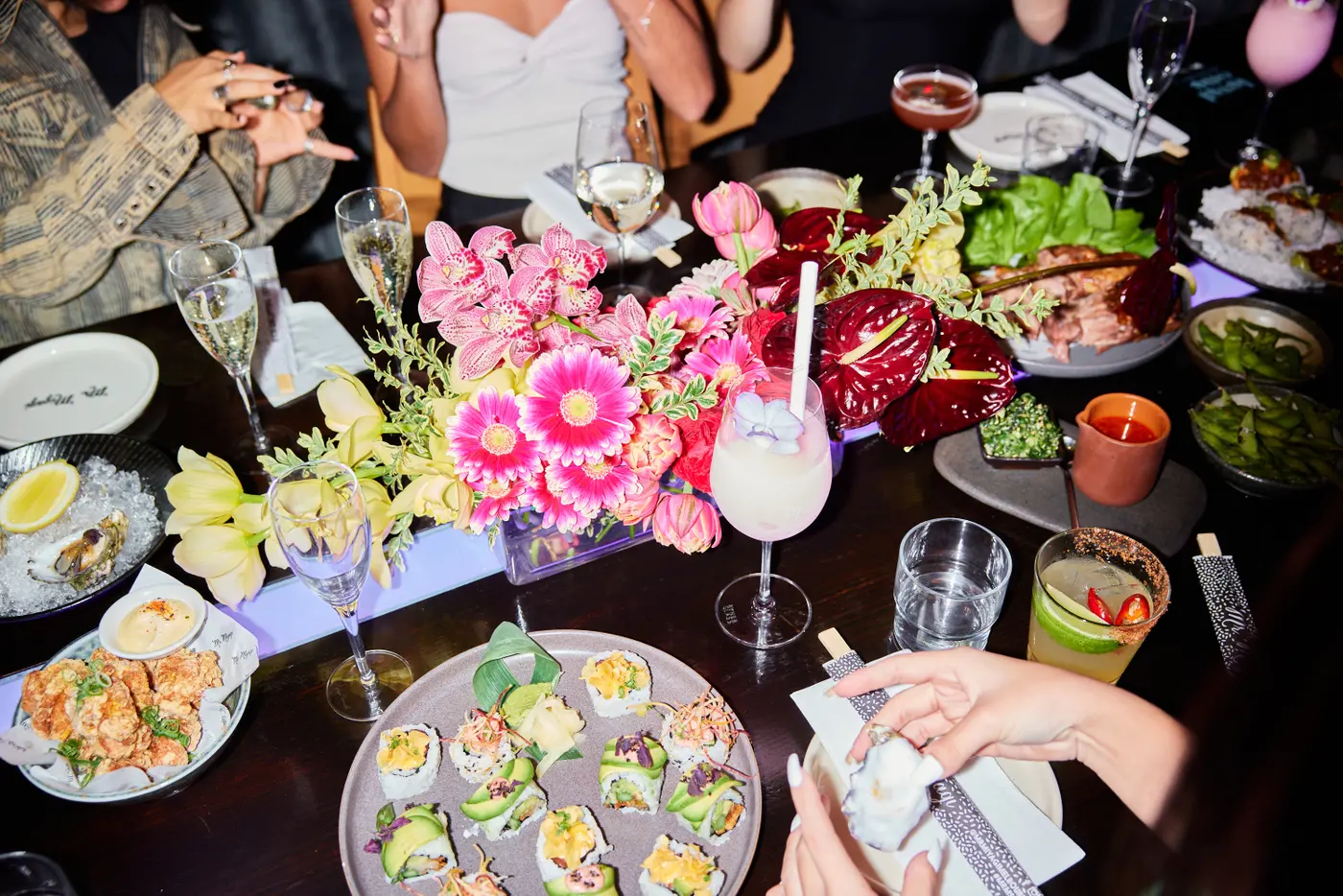 Share plates, cocktails and bright pink flowers on a table surrounded by guests