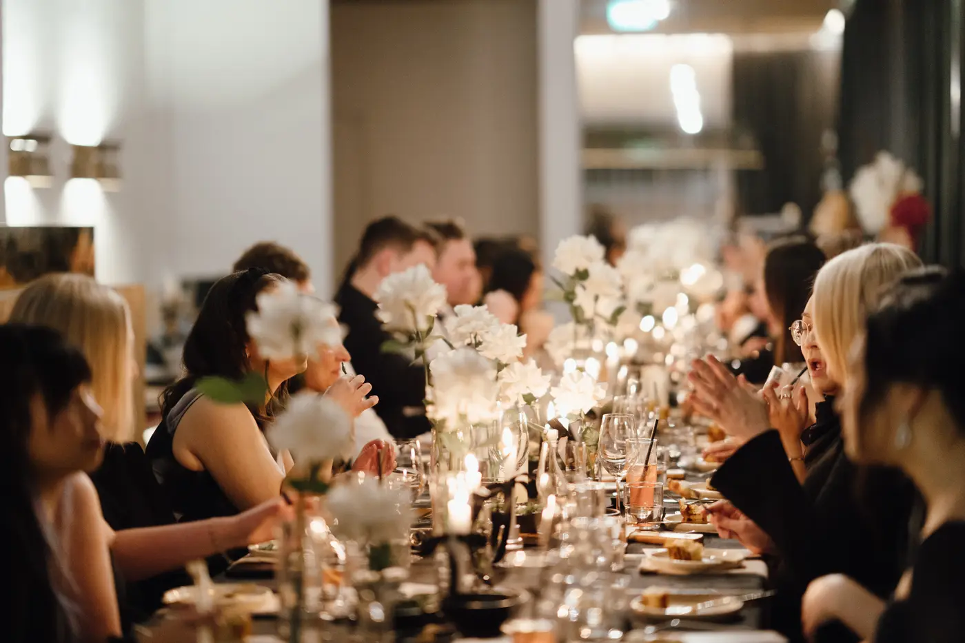 Guests dining together at a long table glowing with warm light