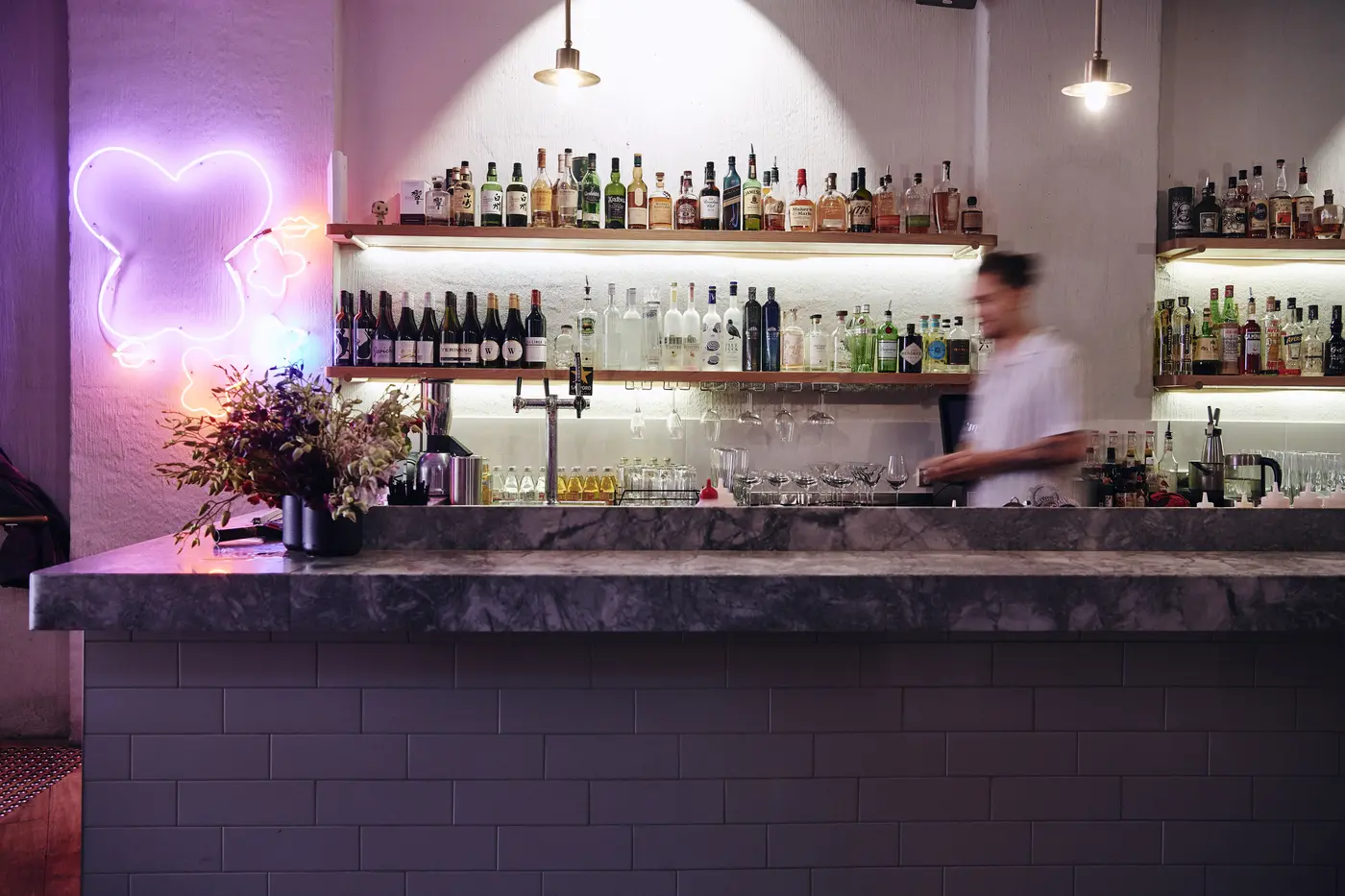 A bartender behind Mr. Miyagi’s bar, lit by a pink neon sign