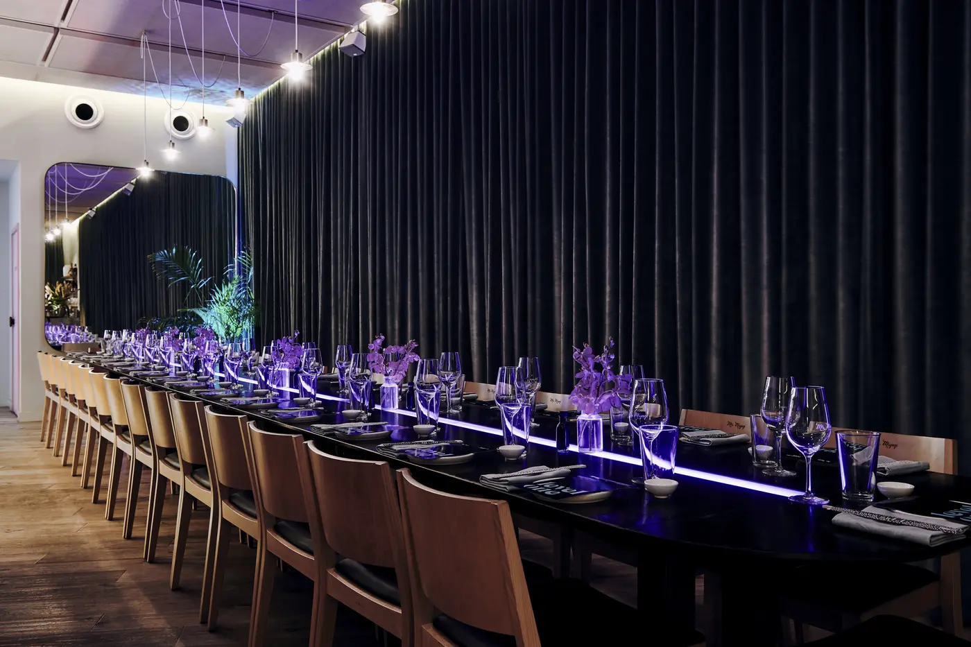 A long dining table set with glassware, tan chairs and dark curtains in Level One
