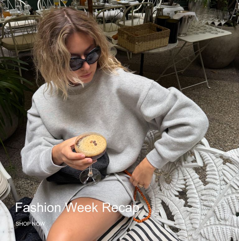 Woman in sunglasses and gray outfit holds a cocktail, sitting on a patterned chair. Text reads "Fashion Week Recap."