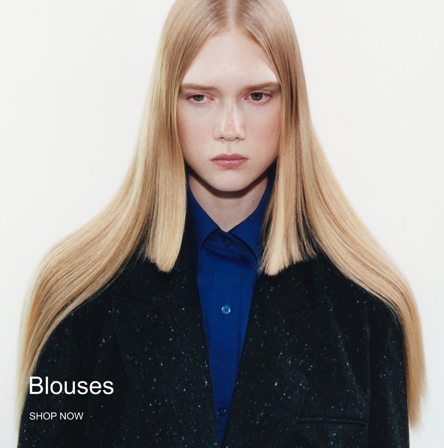 Person with long, straight blonde hair wearing a blue shirt and dark coat. Text reads "Blouses, SHOP NOW."