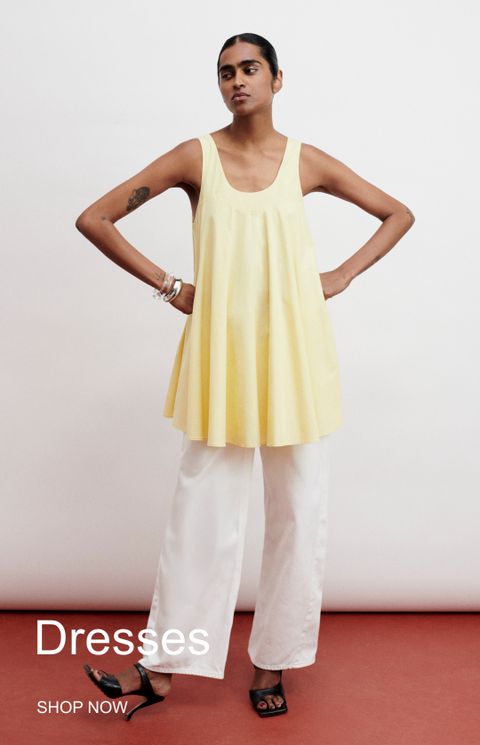 Person in a yellow sleeveless top and white pants poses confidently; text reads "Dresses, Shop Now."