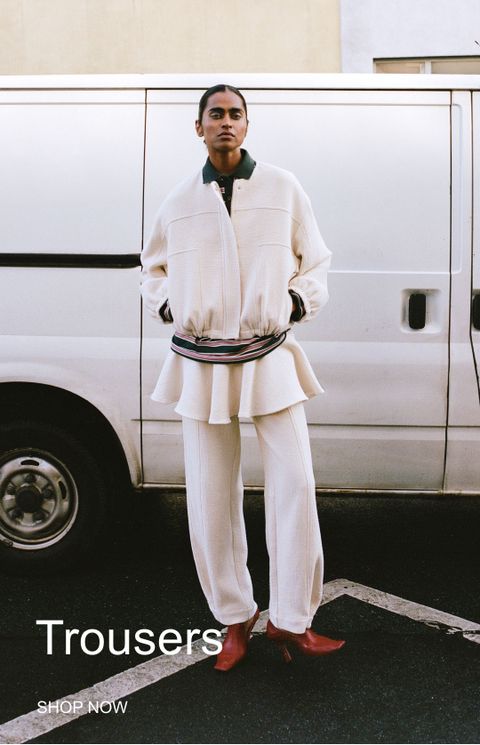 Person in a white outfit with red shoes stands in front of a white van. Text reads "Trousers SHOP NOW."