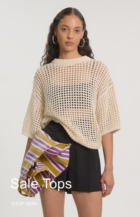 Woman in a cream crochet top and black shorts, holding a striped fabric, with text: "Sale Tops, Shop Now".