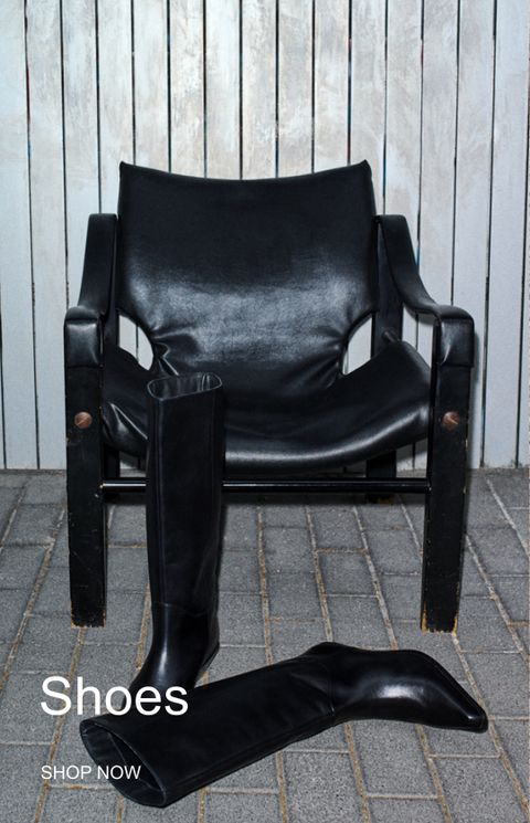 A pair of black leather boots is placed in front of a black leather chair against a wooden panel wall. Text overlay reads "Shoes" and "Shop Now."
