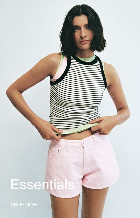 Woman in a striped sleeveless top and pink shorts, posing in a minimal setting. Text reads "Essentials SHOP NOW."