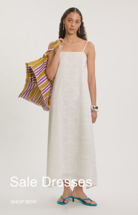 Model in a white, patterned sundress, holding a colorful striped bag, wearing turquoise sandals. Text reads "Sale Dresses, Shop Now."