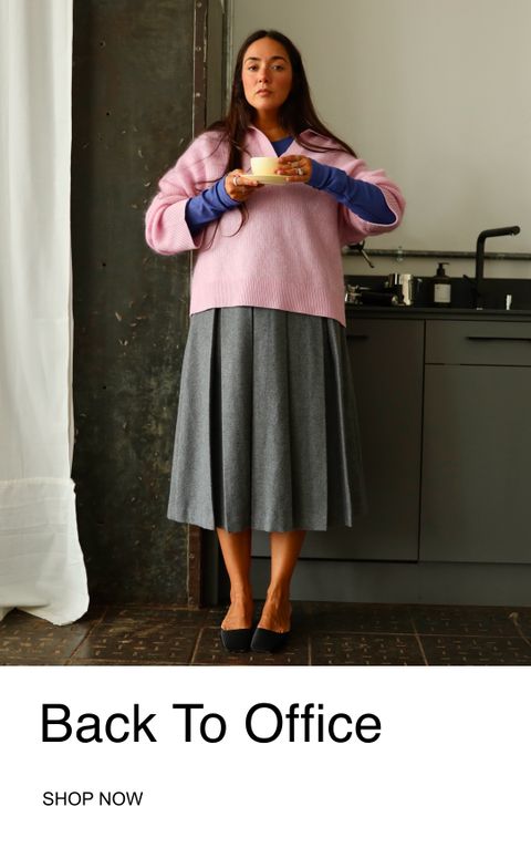 A woman in a pink sweater and gray skirt stands in a kitchen holding a cup. Text reads "Back To Office, Shop Now."