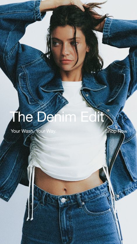Woman wearing a denim jacket and jeans with a white ruched top, posing with arms raised against a plain background. Text overlay reads "The Denim Edit."