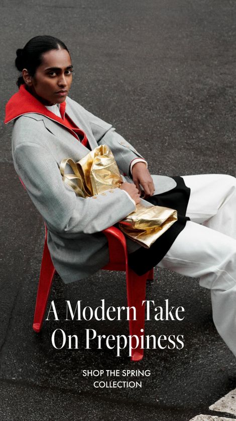 A person in a blazer and wide-leg pants sits on a red chair in a parking lot, holding a gold pouch. Text reads, "A Modern Take On Preppiness."