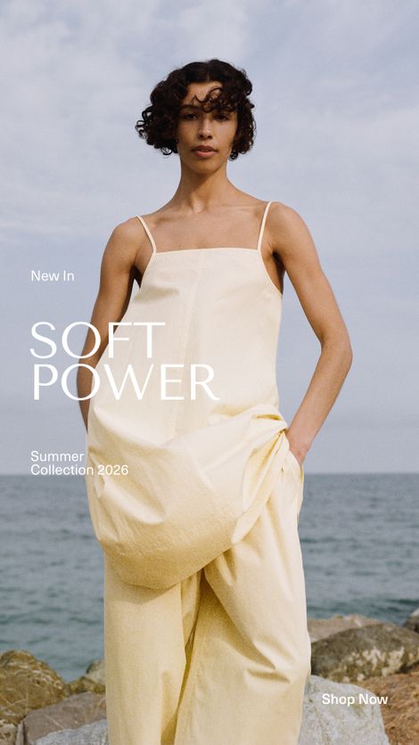 Model in a flowing yellow dress poses by the sea; text reads "SOFT POWER, Summer Collection 2026." Blue sky and ocean in the background.