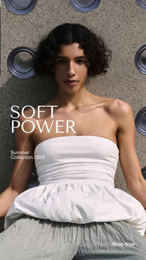 Model in white strapless top and gray skirt sits against textured wall. Text reads "Soft Power, Summer Collection 2026. Shop Now."