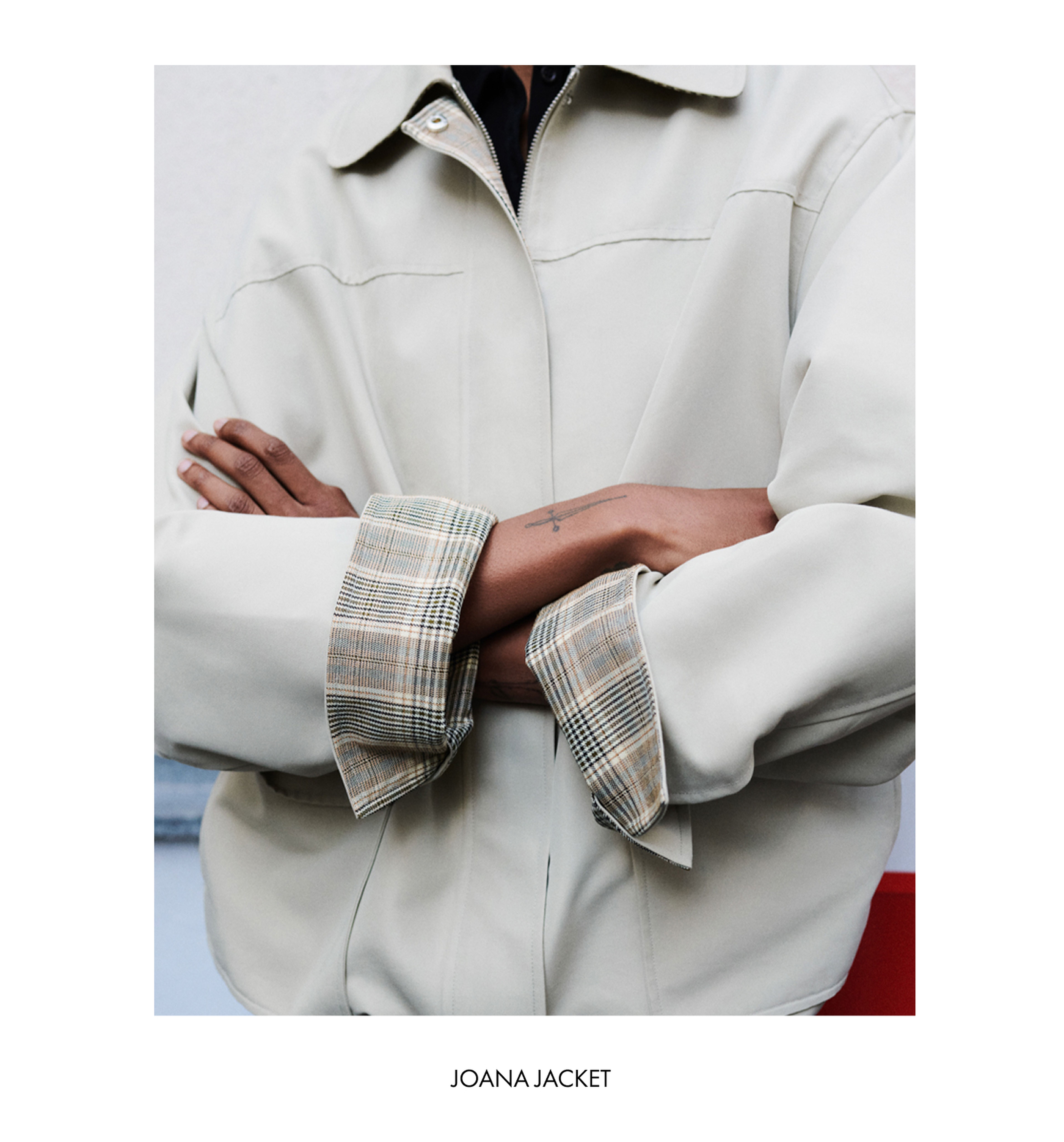 Person wearing a beige jacket with plaid inner cuffs, arms crossed. Text at the bottom reads "JOANA JACKET."