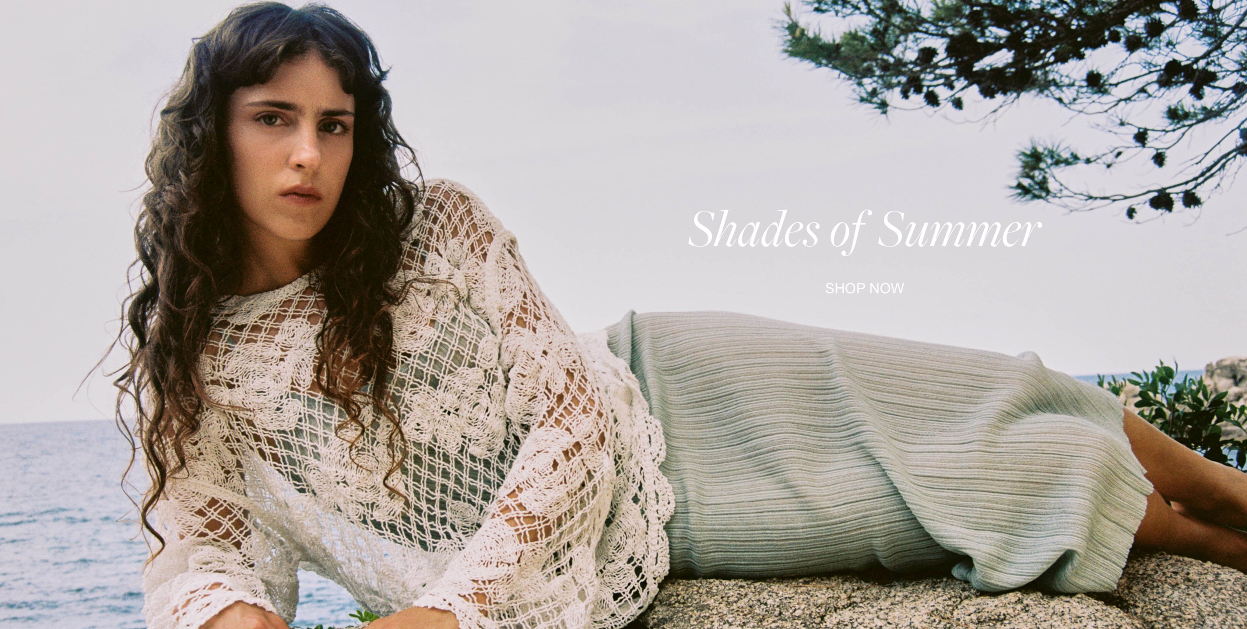 Woman in a lace top and knit skirt reclines on a rock by the sea, with "Shades of Summer" text overlay.