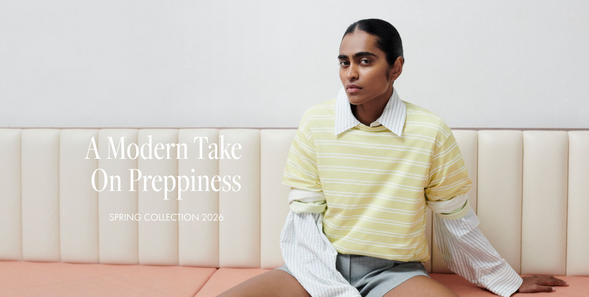 Person wearing layered pastel clothing sits on a cream couch. Text reads "A Modern Take On Preppiness, Spring Collection 2026."