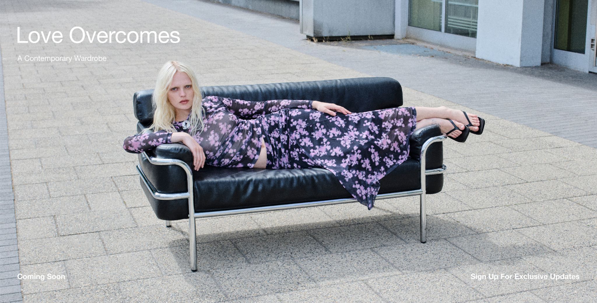 A person in a purple floral dress lounges on a black leather sofa outdoors, next to text that reads "Love Overcomes: A Contemporary Wardrobe."