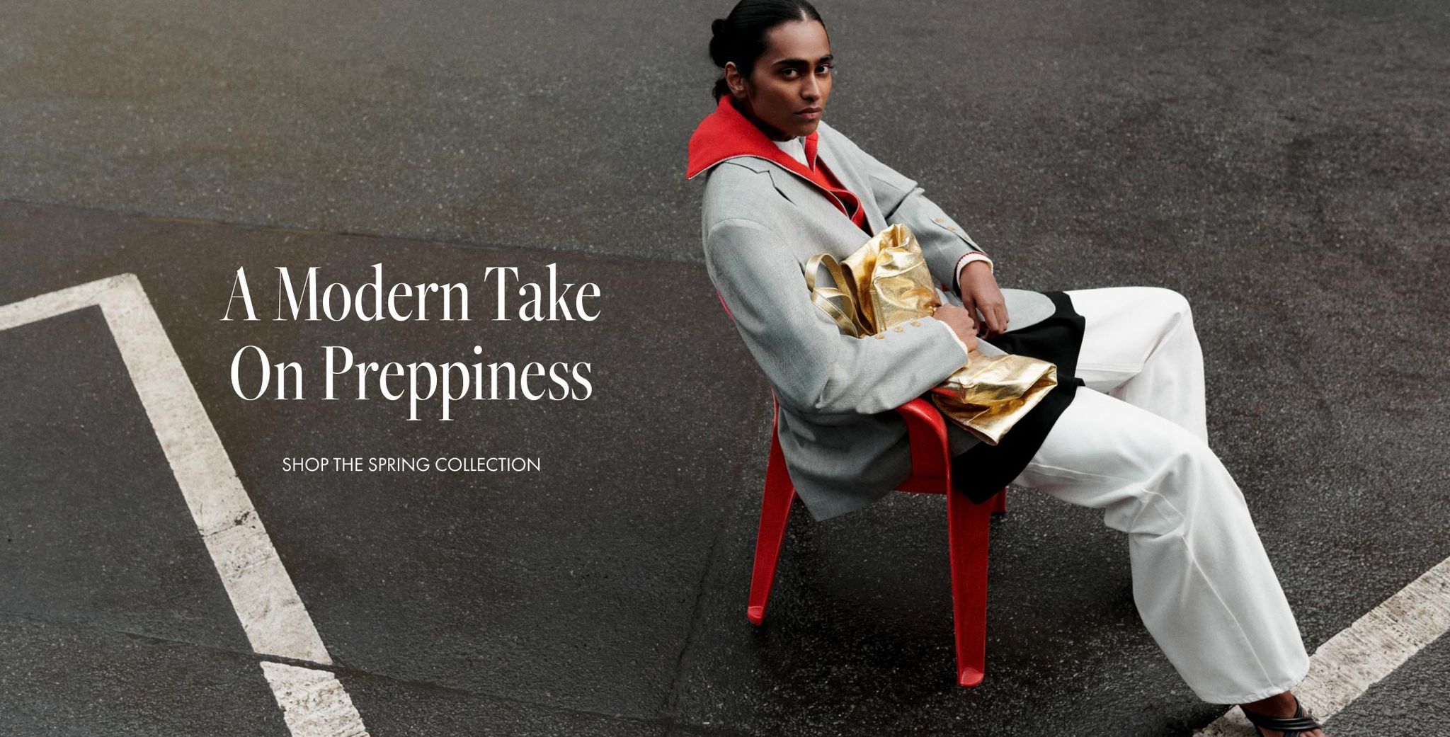 A person in a blazer and wide-leg pants sits on a red chair in a parking lot, holding a gold pouch. Text reads, "A Modern Take On Preppiness."