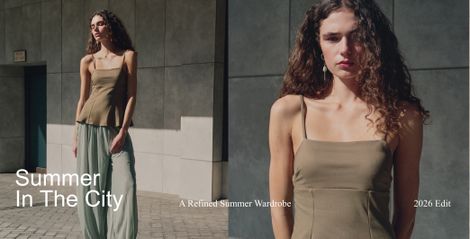 A woman with curly hair wearing a green top and light pants poses in sunlight against a concrete wall. Text reads "Summer In The City" and "2026 Edit."